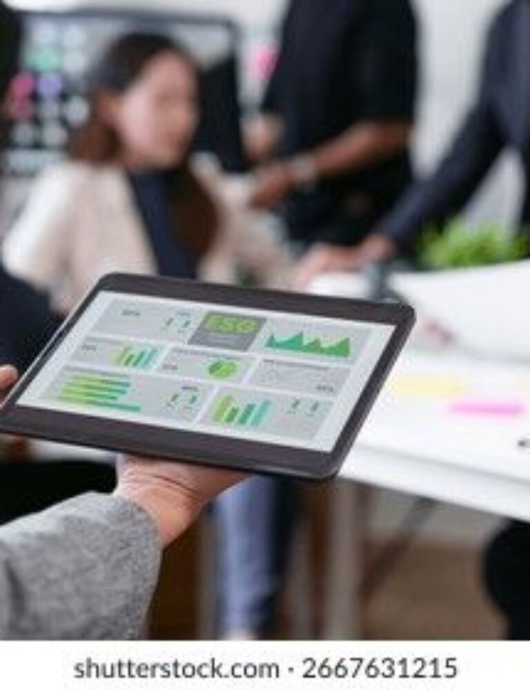 En person holder en tablet med virksomhedsoplysninger og grafer i et kontorlandskab.